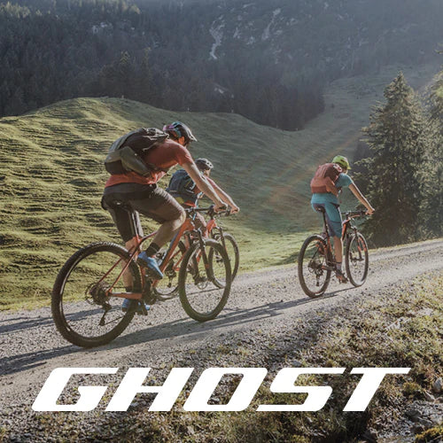 Drei Radfahrer fahren mit ihren Mountainbikes auf einem Schotterweg durch ein malerisches, sonnenbeschienenes Tal mit grünen Hügeln und Kiefern, mit dem Wort GHOST in fetten weißen Buchstaben am unteren Rand.