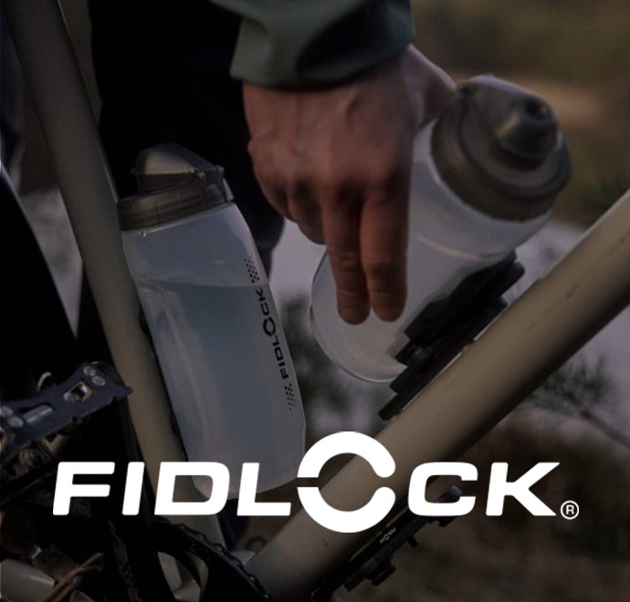 Eine Person befestigt eine Fidlock-Wasserflasche mit einer Magnethalterung an einem Fahrradrahmen. Das Fidlock-Logo ist am unteren Rand des Bildes gut sichtbar angebracht.