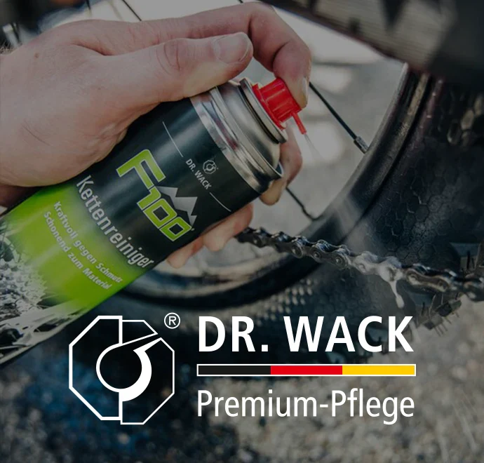 Eine Hand sprüht Dr. Wack F100 Kettenreiniger auf eine Fahrradkette. Im Vordergrund erscheinen das Dr. Wack-Logo und der Text Premium-Pflege.