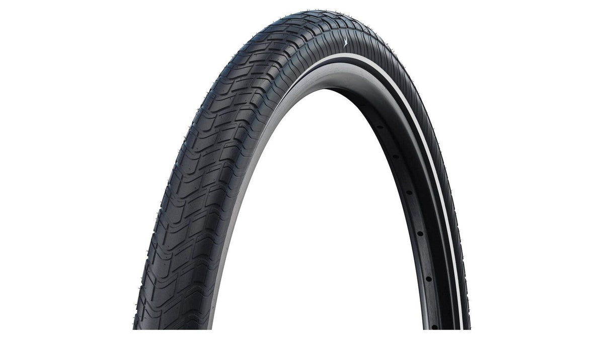 Eine Nahaufnahme des SCHWALBE Motion Big Apple 20" Reifens zeigt sein dezentes Profil und die Seitenwand vor einem weißen Hintergrund. Der schwarze Schwalbe-Reifen ist leicht geneigt, was das Profil hervorhebt.